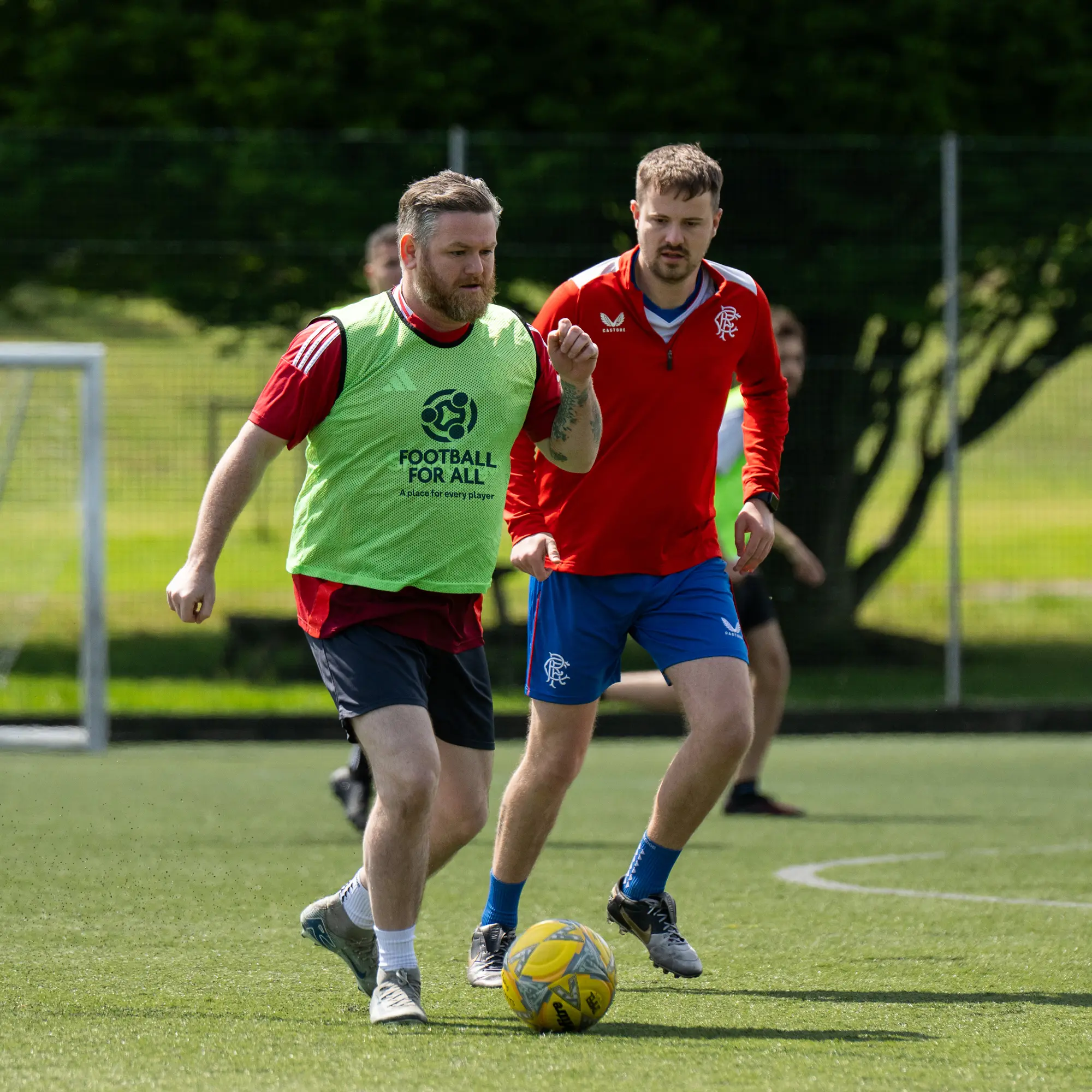 Adults in bibs playing friendly local football games on an outdoor pitch